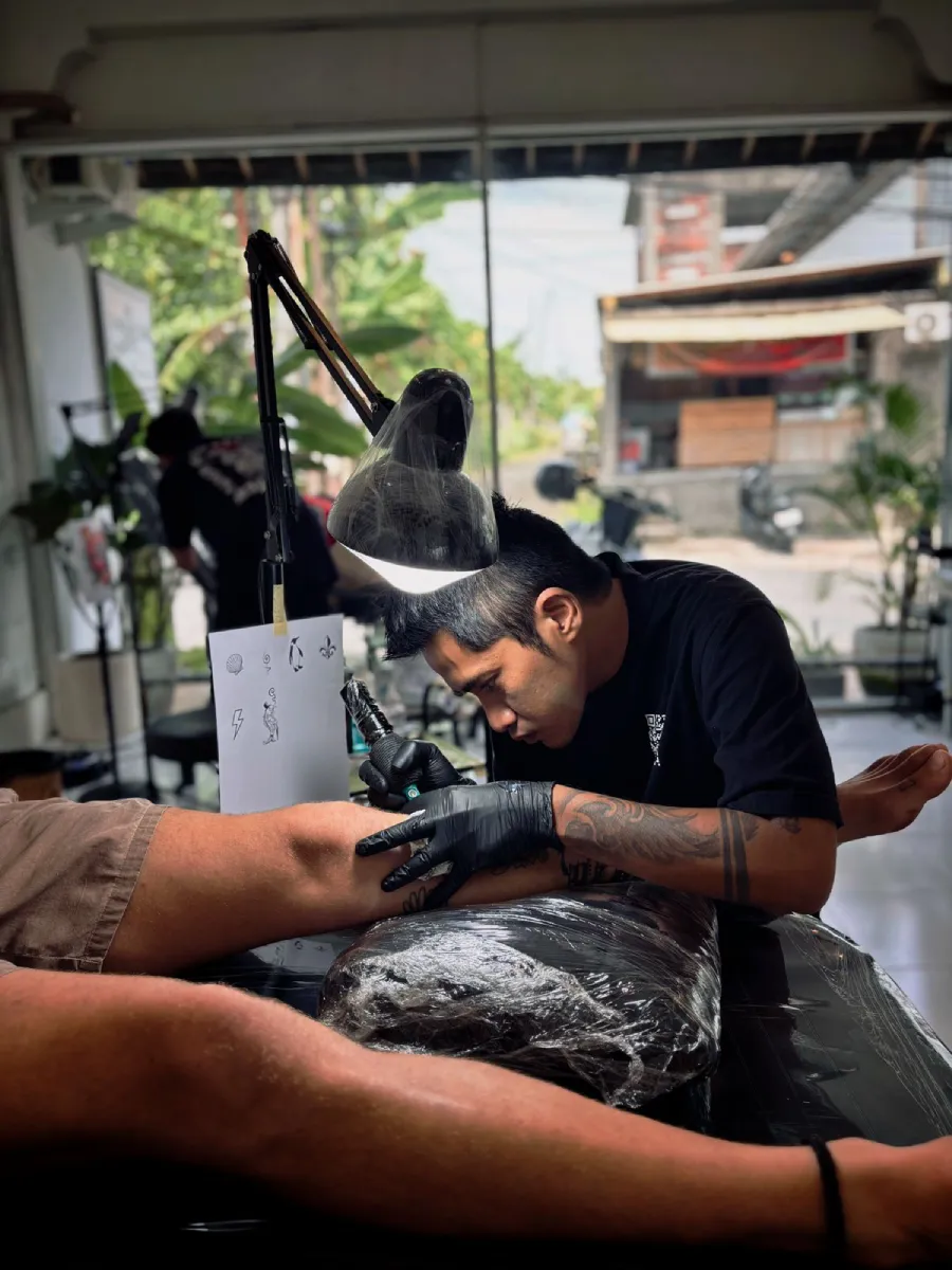 Female client getting fine line arm tattoo under clinic lamp